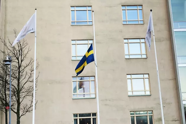 Tre flaggstänger utanför Campus Helsingborg med en svensk flagga på halvstång. Foto.