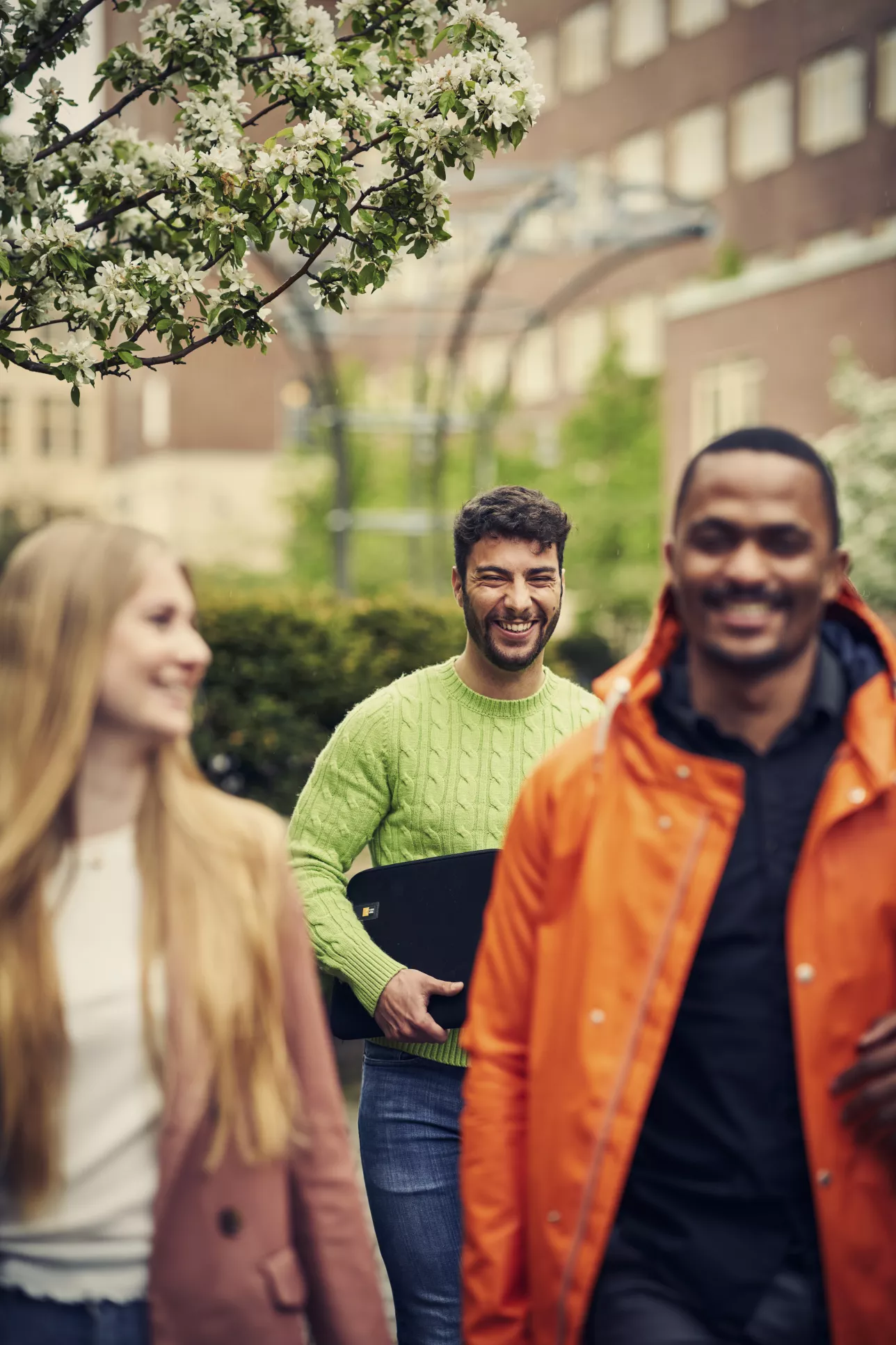 Tre leende studenter gåendes inne på Campus Helsingborgs innergård. Foto.