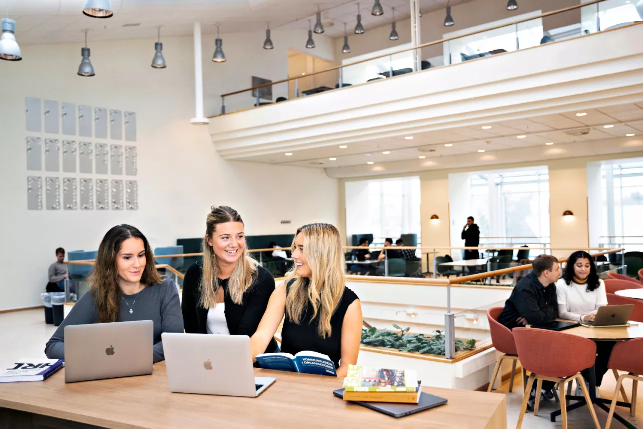 Tre studenter sitter med datorer. Foto.